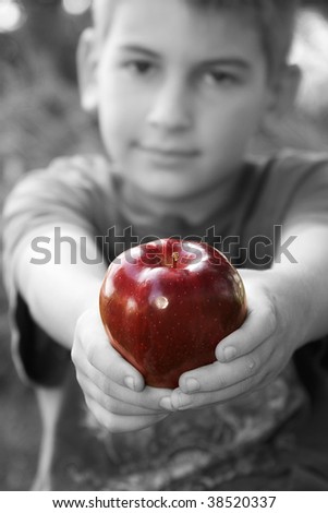 Black and white photo of young boy holding out in front red apple, focus on apple.
