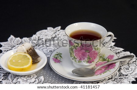 Tea cup sitting on lace doily with spoon and tea bag with lemon to the side