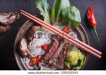 Vietnamese Pho Bo soup served in vintage oriental bowl with chop sticks, seasoning and greens on background