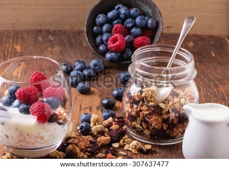 Home Made Granola breakfast with white plain yogurt, blueberries, raspberries and dry cherries on rustic wooden background, selective focus