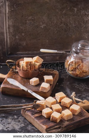 Rustic wooden boards with fudge candy glass sugar bowl, served with sugar cubes over dark background