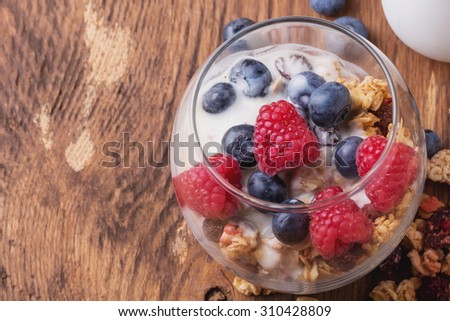 Home Made Granola breakfast with white plain yogurt, blueberries, raspberries and dry cherries on rustic wooden background