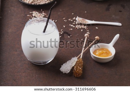 A glass of home made rice milk served with brown rice, honey and organic sugar candies on a rustic metal background