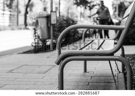 Park bench in city center. Photo was taken in Szeged, Hungary. Selective focus. The bench is madeof iron and wood. Black and white.