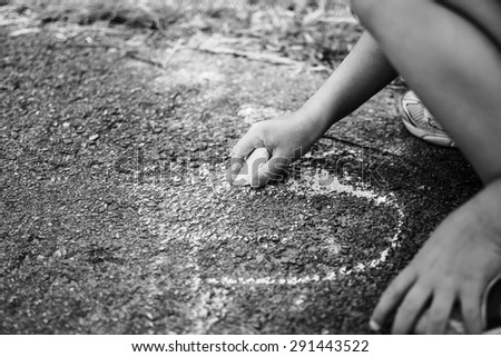 Children draw in the park with chalks of various colors. Black and white photo. Selective focus on hand.