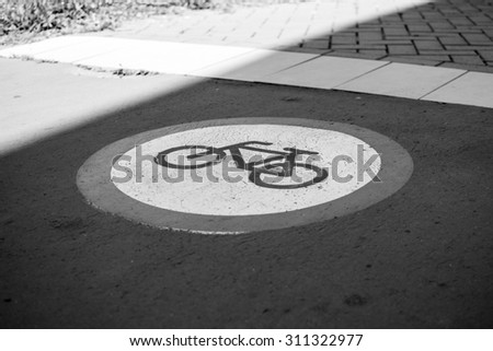 Bicycle path sign on the street. Photo was taken on a nice sunny day. Summer time. Focus is on the middle of the sign. Black and white photo.