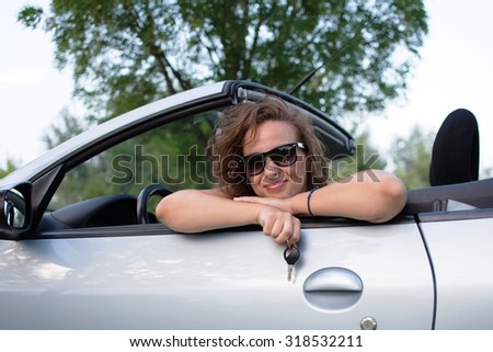 Beautiful young woman in a convertible car, with car key in hand.
