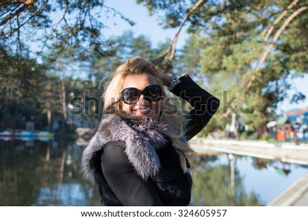 Beautiful young woman with long blonde hair, smiling. Wearing black glasses. Nature background.