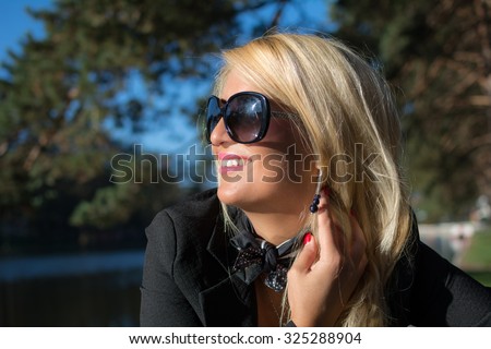 Portrait of a young beautiful woman with long blond hair and black glasses in park. Photographed was taken on a nice sunny day. Nature background.