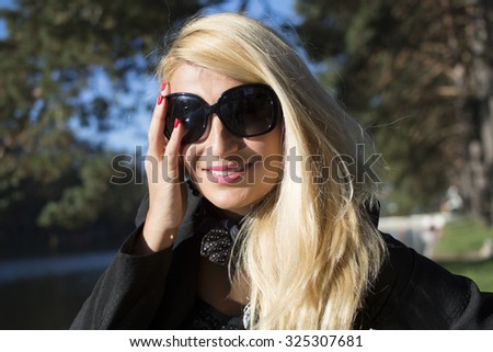 Portrait of a young beautiful woman with long blonde hair,red nails and black glasses in park. Photographed was taken on a nice sunny day. Nature background.
