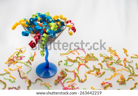 Stylish martini glass filled with colorful decorative ribbon and crinkle-cut confetti on a white tablecloth