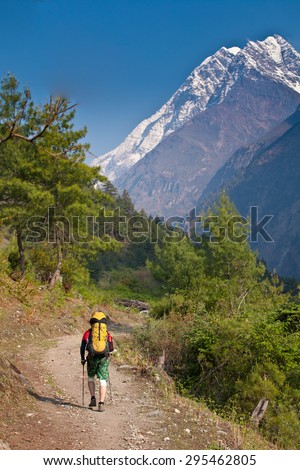 Nepal - man on hiking trail in mountains. Background - mountain lodge and snow peak