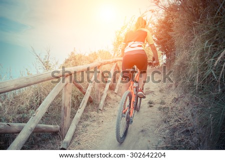 girl stands up to pedal along a steep climb. a ride to a woman in the hills in close contact with nature. Cyclist pedaling uphill with a backdrop of the sea at sunset.