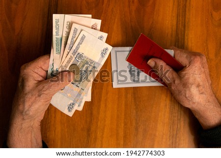 Elderly man holding russian ruble banknotes in one hand and pension certificate with passbook
in another. The concept of pension, payment and money savings.