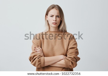 Waist-up portrait of beautiful girl with blonde straight hair frowning her face in displeasure, wearing loose long-sleeved sweater, keeping arms folded. Attractive young woman in closed posture. Сток-фото © 