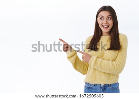 Excited and surprised young happy woman in yellow sweater, drop jaw gasping in awe and astonished pointing looking left side blank space for your promo, standing white background fascinated Foto stock © 
