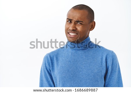 Ouch that hurts. Portrait of embarrassed and awkward young man cringe, grimacing and looking pity camera, feel discomfort trying to say something with caution, white background Foto stock © 