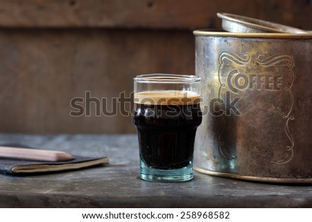 coffee in glass cup on table with rusted tin box and notebook and pencil