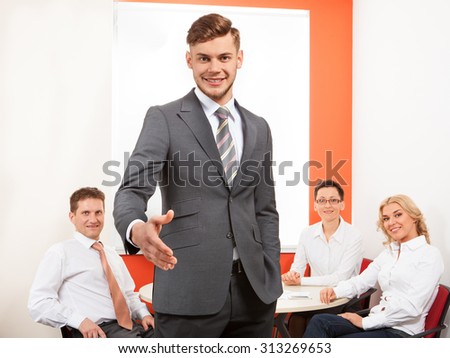 Portrait of happy businessman offering handshake and his team in office