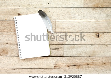 notebook and feather on wood table with soft light, space for text