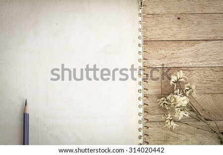 Blank note book paper, pencil and dry flower on wooden background, vintage fade tone and vignetting