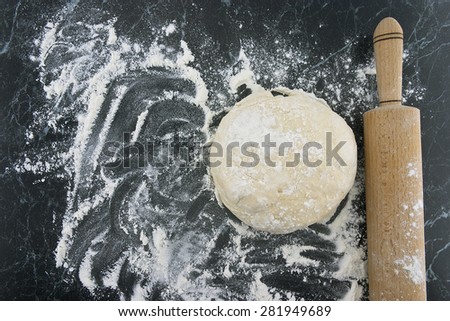 Freshly prepared dough on a wooden board. Rolling pin and flour on table. Top view.