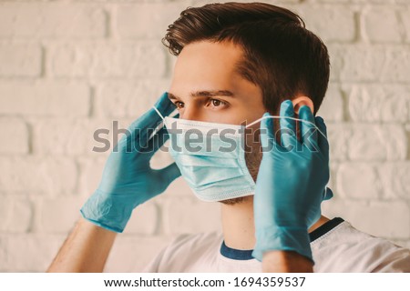 Confident young surgeon doctor in latex protective gloves wearing medical mask on face. Man professional medic in medical gloves put on protective face mask. Personal protection. Coronavirus COVID-19 Foto stock © 