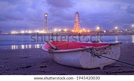 A boat on the beach at the end of the day after bad weather with the great mosque of Algiers and a big wheel in the background Foto stock © 