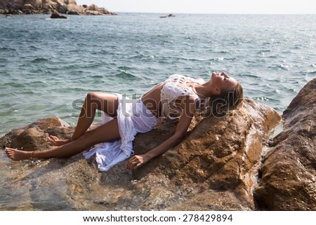 Sexy lady in wet white lace dress on rocky coast.
