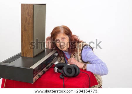 Elderly woman with the hand on her ear, trying to hear radio