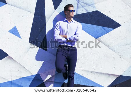 Young handsome business  man in blue  suit and glasses watching against painted wall