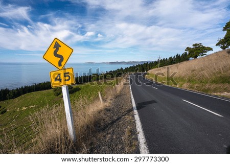 Empty Road by the bay with speed limit and winding road sign in New Zealand.