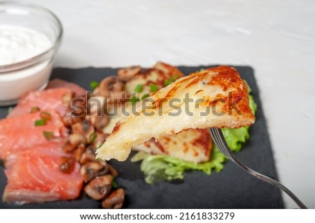 a traditional Swiss dish is strung on a fork - part of a potato pancake. in the background, you can see the food on the board for serving dishes. Imagine de stoc © 