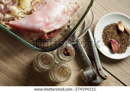 raw rabbit meat in roaster with onion cumin and garlic on wooden vintage table