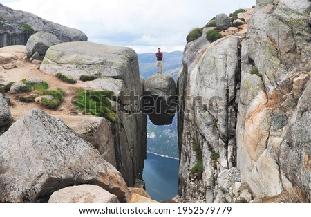 A brave hiker stands on the Kjeragbolten, a colossal boulder wedged between two rock faces, overlooking the Lysefjord in Norway 商業照片 © 