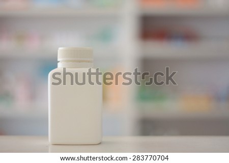 Blank white medicine bottle with blur shelves of drug in the pharmacy drugstore background
