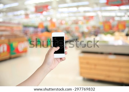 Closeup of a woman\'s hand holding a smart phone in Supermarket blurred background, business concept