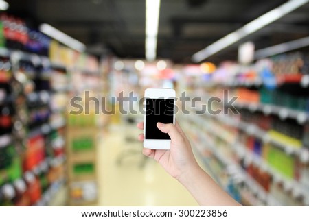 Closeup of a woman\'s hand holding a smart phone in Supermarket blurred background, business concept
