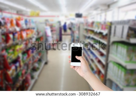 hand holding smartphone with convenience store shelves blurred background