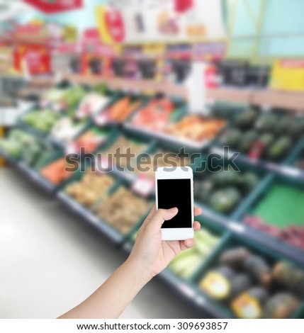 Hand holding mobile phone with Vegetables and fruit on shelf in supermarket blurred background