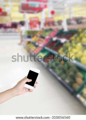 Hand holding mobile phone with Vegetables and fruit on shelf in supermarket blurred background