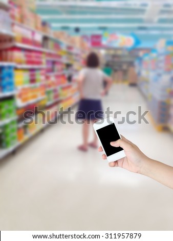 hand holding smartphone with female shopping in supermarket background