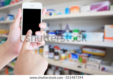 pharmacist hand holding smart phone with blur some shelves of drug in the pharmacy drugstore