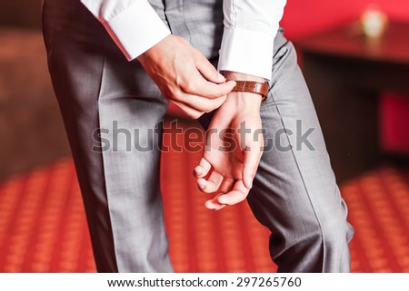 A groom putting on cuff-links as he gets dressed in formal wear .Groom's suit