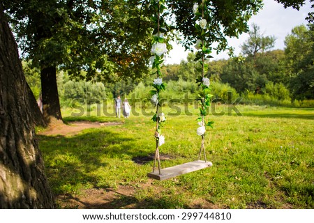 Old wooden vintage garden swing hanging from a large tree on green grass background, in golden evening sunlight