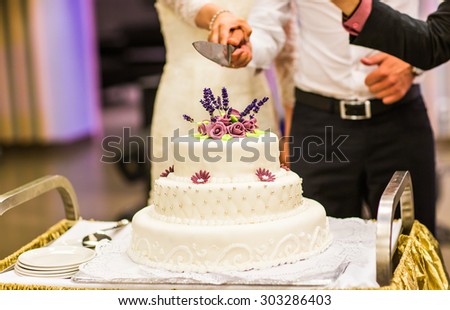 a multi level white wedding cake on a silver base and violet flowers of sugar