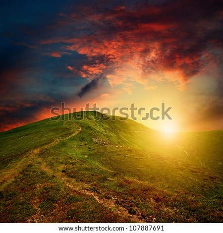 amazing mountain sunset with red clouds over the green hill
