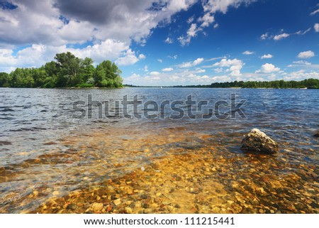 River bottom with stones in transparent water. Green island on cloudy sky background