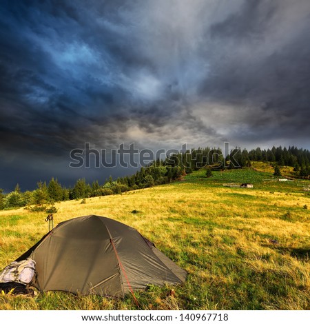 touristic tent and dark storm clouds over hill with pine trees