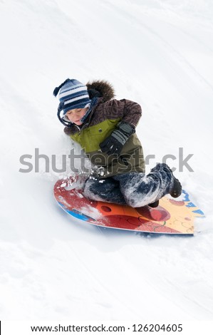 young boy tobogganing and falling off